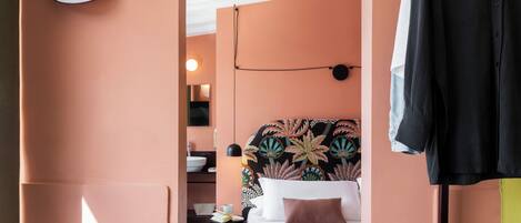 A hotel room with a bed, a desk, a chair, and a hanging coat rack.