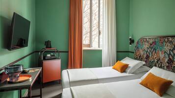 Ein Hotelzimmer mit zwei Betten, einem Schreibtisch mit Wasserkocher, einem Spiegel und einem Fenster mit Vorhängen.