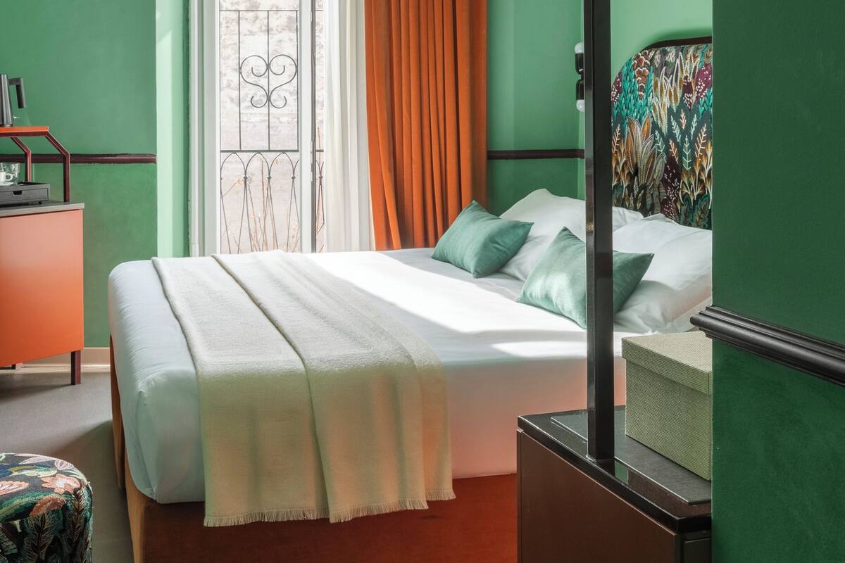 A bedroom with a bed, a window with curtains, a dresser, and a mirror.