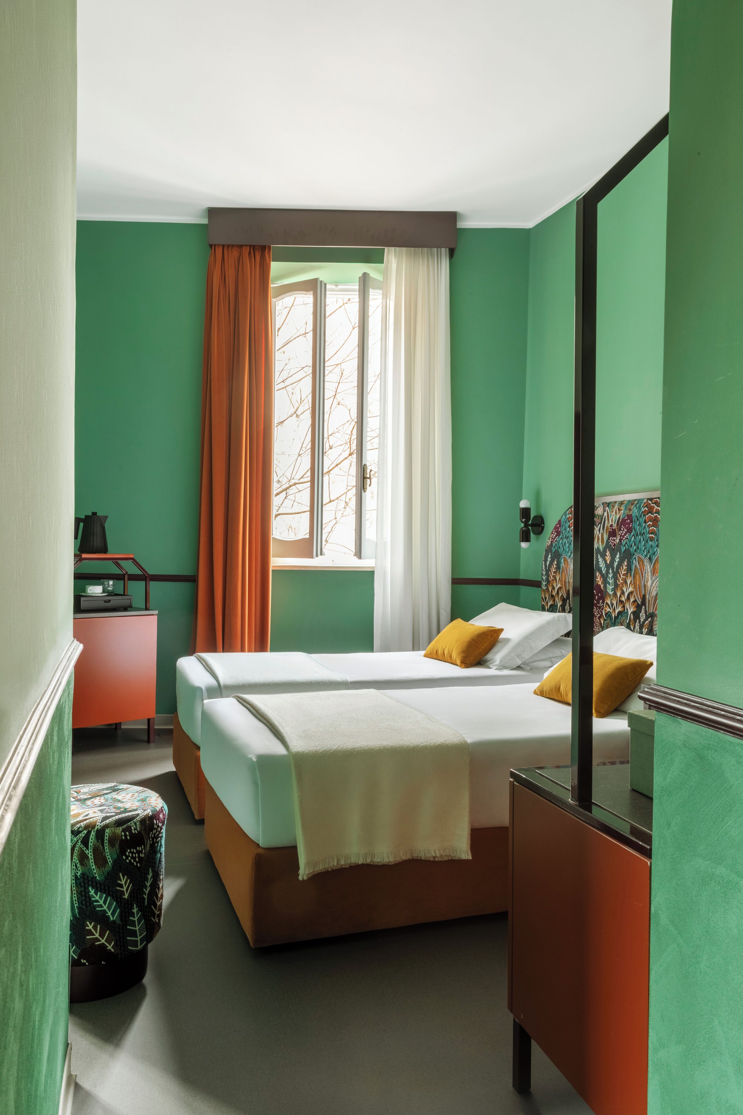 A room with a bed, a desk, a chair, a window with curtains, and a mirror.