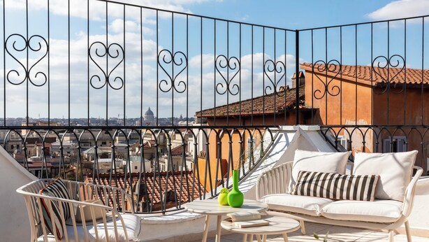 Un balcon avec un canapé blanc, une chaise blanche et une petite table sur laquelle se trouve un vase vert.
