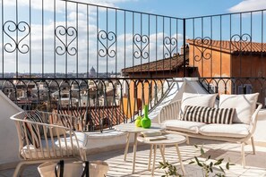 En balkon med en hvid sofa, en hvid stol og et lille bord med en grøn vase.