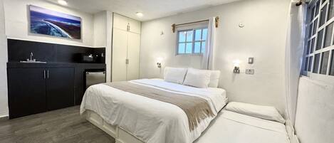 A bedroom with a bed, a small desk, a window, and a painting on the wall.