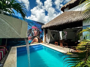 A swimming pool with a mural, a thatched-roof structure, and tropical plants.