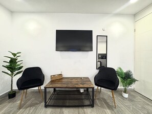 A modern room with a wooden table, two black chairs, a TV, and two potted plants. - La Perle Noire | AB - Terasse et Piscine (San Miguel de Cozumel)