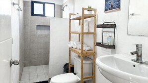 Un baño con ducha, inodoro, lavabo y un estante de madera con toallas.