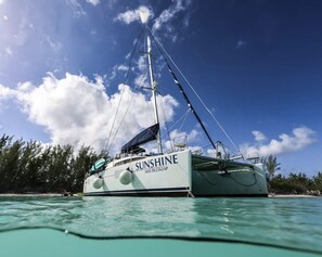 A sailboat named 'SUNSHINE' with a registration number 'MAT DL2362AP' anchored in clear turquoise waters.