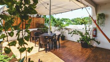 Ein Terrassenbereich im Freien mit einem Holztisch und -stühlen, umgeben von Topfpflanzen und einer Hängelampe.