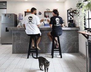 Una cocina moderna con dos personas sentadas en una barra, un gato en el suelo y varios electrodomésticos.