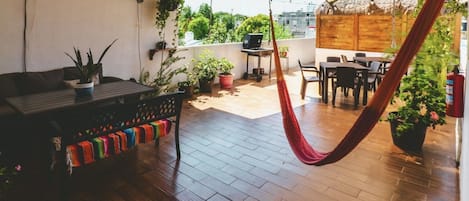An outdoor patio with a hammock, wooden flooring, a dining area, and potted plants.