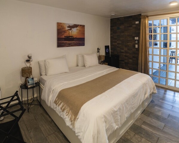 Un dormitorio con una cama grande, un cuadro en la pared, una ventana con cortinas y una mesita de noche con lámpara.