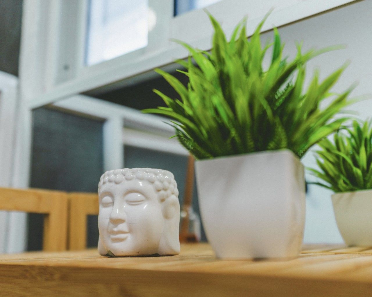 Eine weiße Buddha-Statue aus Keramik steht auf einem Holztisch, neben ihr ein Blumentopf.