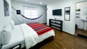 A bedroom with a bed, a TV, a desk, and a bathroom. - La Perle Noire | HM - Terrace and Pool (San Miguel de Cozumel)