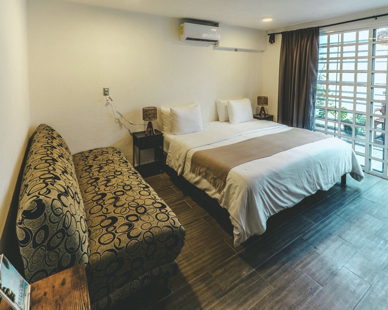 A hotel room with a bed, a sofa, a nightstand, and a window with curtains.