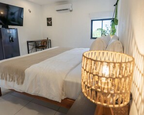 Un dormitorio con cama, televisión, aire acondicionado, ventana y una silla.