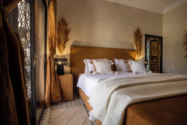 A bedroom with a large bed, a nightstand, a lamp, and decorative plants. - Just V hotel & Spa  (Oulad Hassoune)