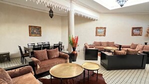 Un ampio soggiorno con soffitto alto, pavimento decorato e zona centrale con divani e tavolini rotondi.