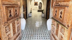 Un corridoio con porte in legno decorate, pavimento piastrellato e un arco centrale che conduce a una stanza.