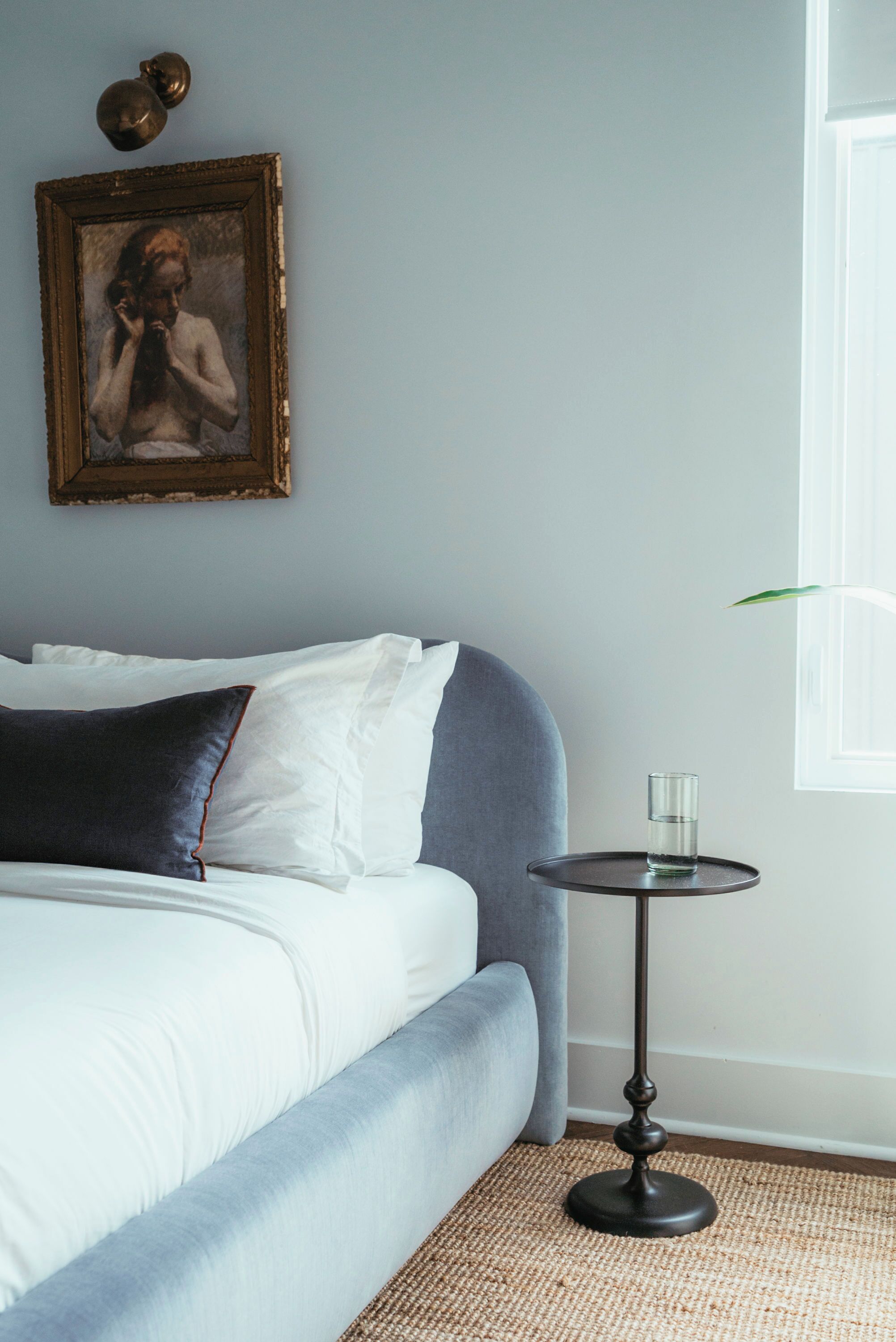 Une chambre à coucher avec un lit, des oreillers, une petite table avec un verre, et un tableau encadré au mur.