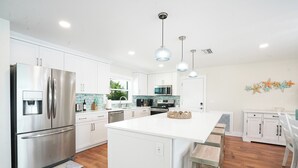 A modern kitchen with white cabinetry, stainless steel appliances, and pendant lighting. - New Waterfront house pool hot tub golf cart kayaks (Indian Rocks Beach)