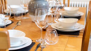 Una mesa de comedor preparada con platos, vasos y cubiertos, rodeada de sillas.