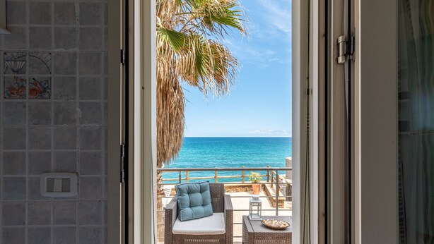 A balcony with wicker furniture, a view of the sea, and a tiled wall. - Villetta Ficarazzi by Wonderful Italy (Ficarazzi)