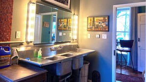 Une salle de bain avec un grand miroir, deux appliques murales, un lavabo et une poubelle.