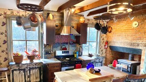 Une cuisine rustique aux murs en briques apparentes, aux poutres en bois et aux ustensiles de cuisine suspendus.