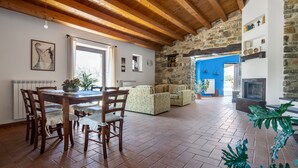 A spacious living area with a stone wall, wooden ceiling beams, a dining table with chairs, and a fireplace. - Villa Granci con Piscina by Wonderful Italy (Polizzi Generosa)