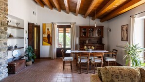 A rustic interior with exposed wooden beams, a dining area with a table and chairs, a bookshelf, and a stone wall with shelves. - Villa Granci con Piscina by Wonderful Italy (Polizzi Generosa)