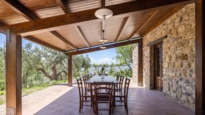 A covered outdoor dining area with a stone wall and wooden beams, overlooking a scenic landscape. - Villa Granci con Piscina by Wonderful Italy (Polizzi Generosa)