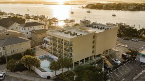 A multi-story hotel with a rooftop pool, a marina in the background, and a parking lot with several cars.