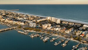 An aerial view of a coastal town with a marina, residential buildings, and a pier extending into the ocean.