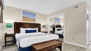Une chambre d’hôtel avec un grand lit, deux tables de chevet, un banc, un miroir et un tableau représentant une scène de plage.