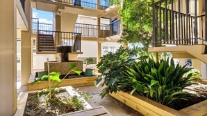 A multi-level outdoor area with wooden planters, a small fountain, and a staircase leading to upper levels. - Summer Sands Diggin' In The Sand Room 103 (Wrightsville Beach)