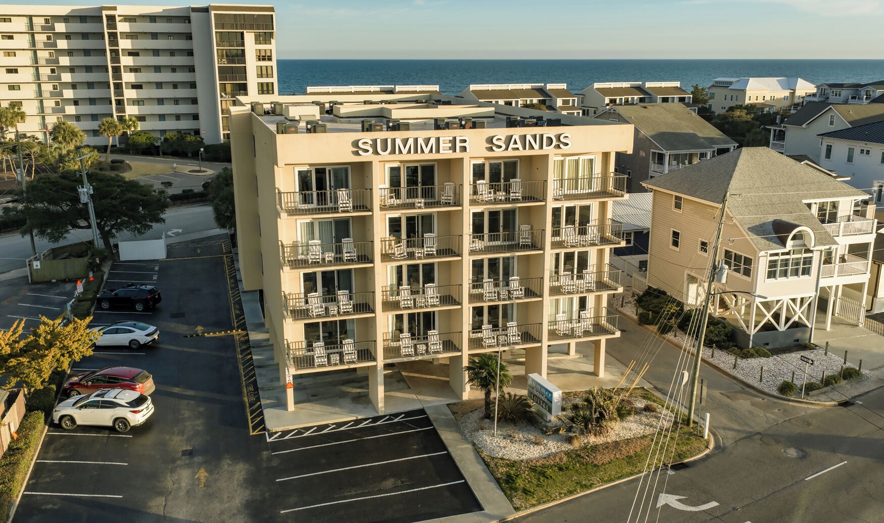 A multi-story hotel named 'Summer Sands' with balconies, a parking lot, and a view of the ocean.
