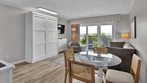 A modern living room with a glass-top dining table, a sofa, and a TV. - Summer Sands- Isle Be Back Room 203 (Wrightsville Beach)