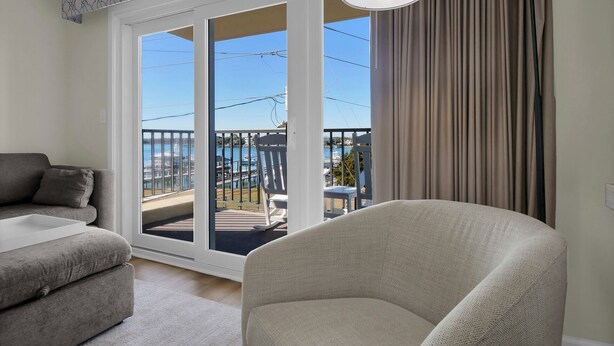 Sala de estar com sofá, poltrona e vista para o mar através de uma porta de correr de vidro.