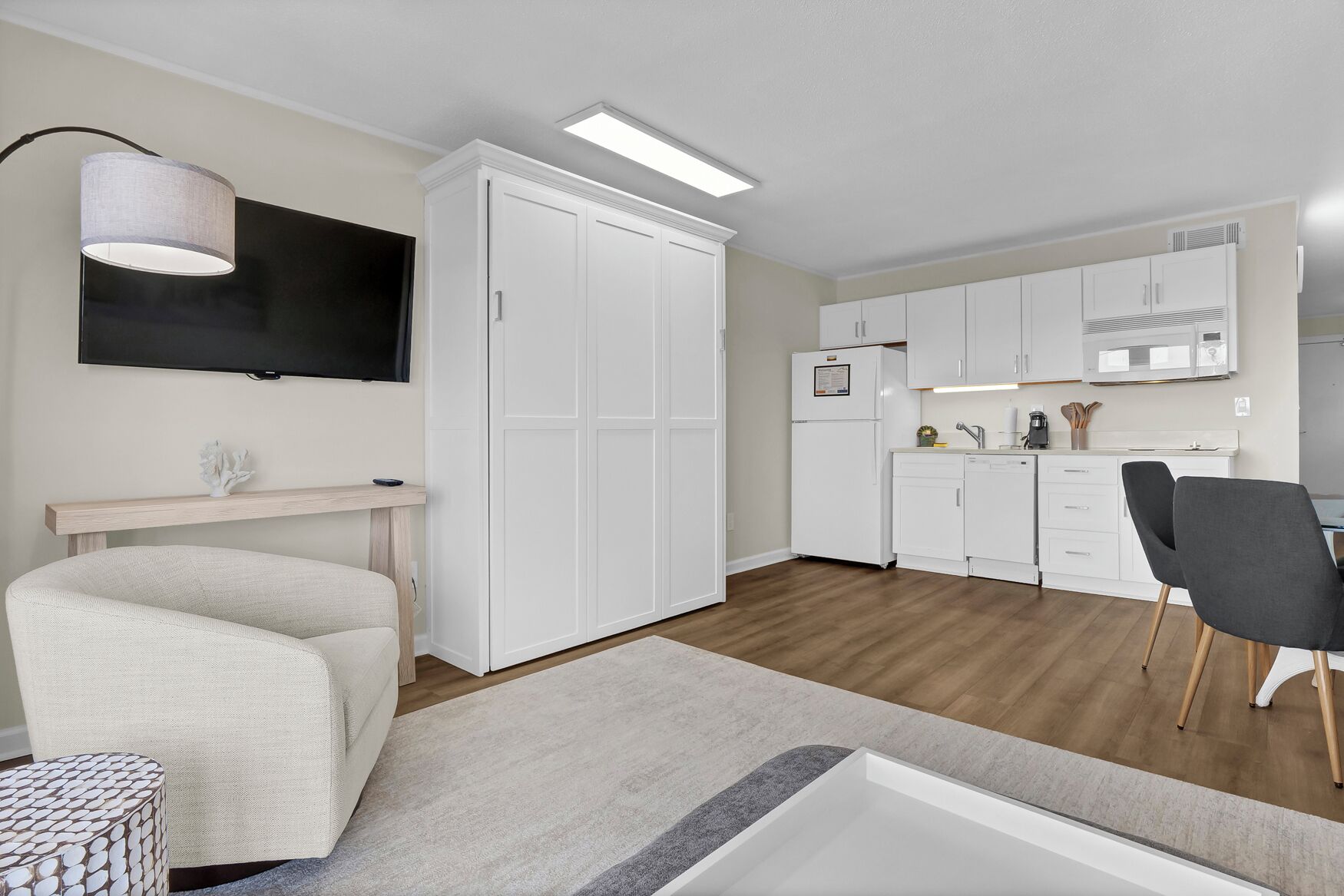 Een moderne, compacte leefruimte met een kitchenette, een flatscreen televisie, een eethoek en een zithoek met een bank en een klein rond tafeltje.