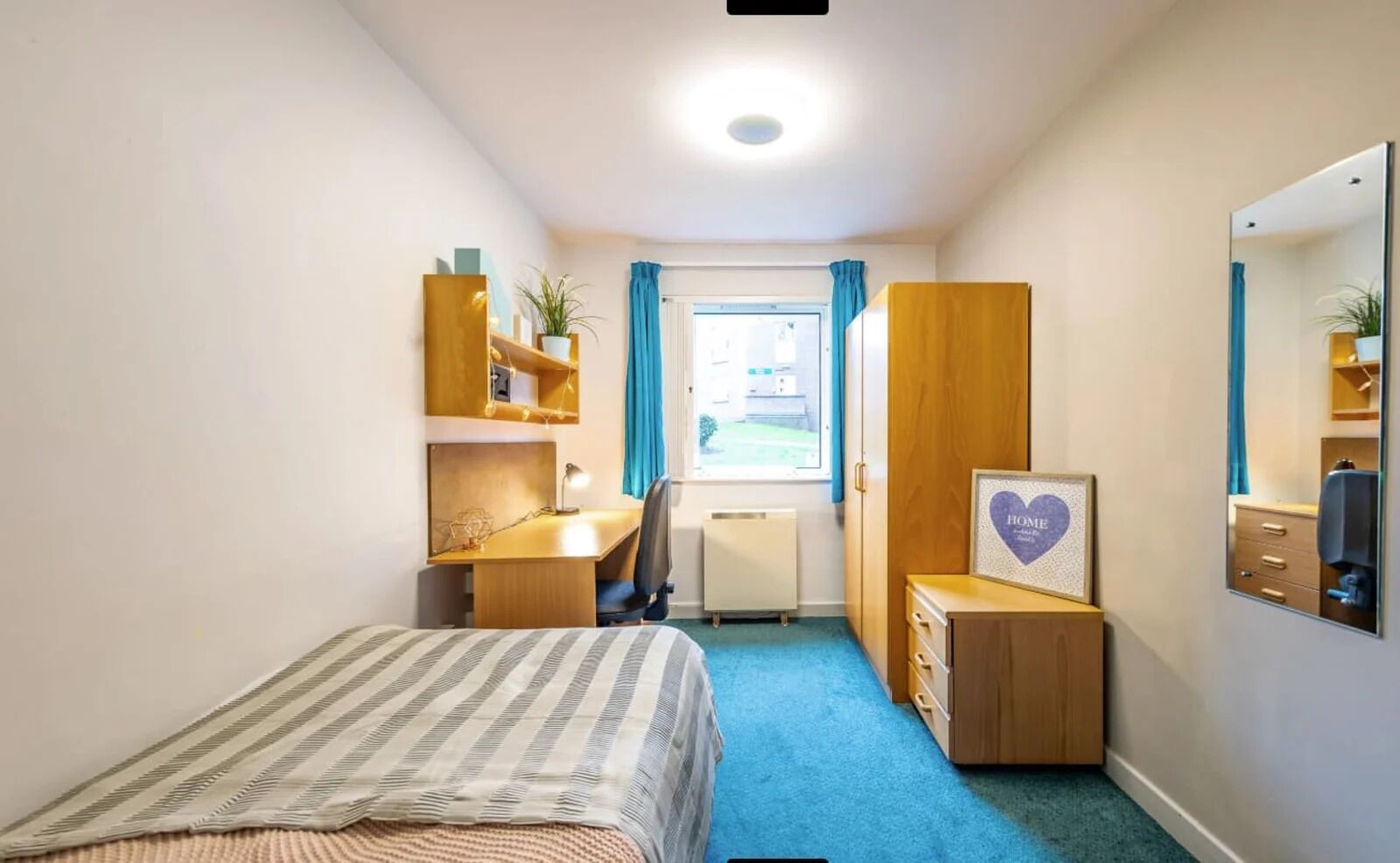 A compact hotel room with a bed, a desk, a wardrobe, and a mirror.