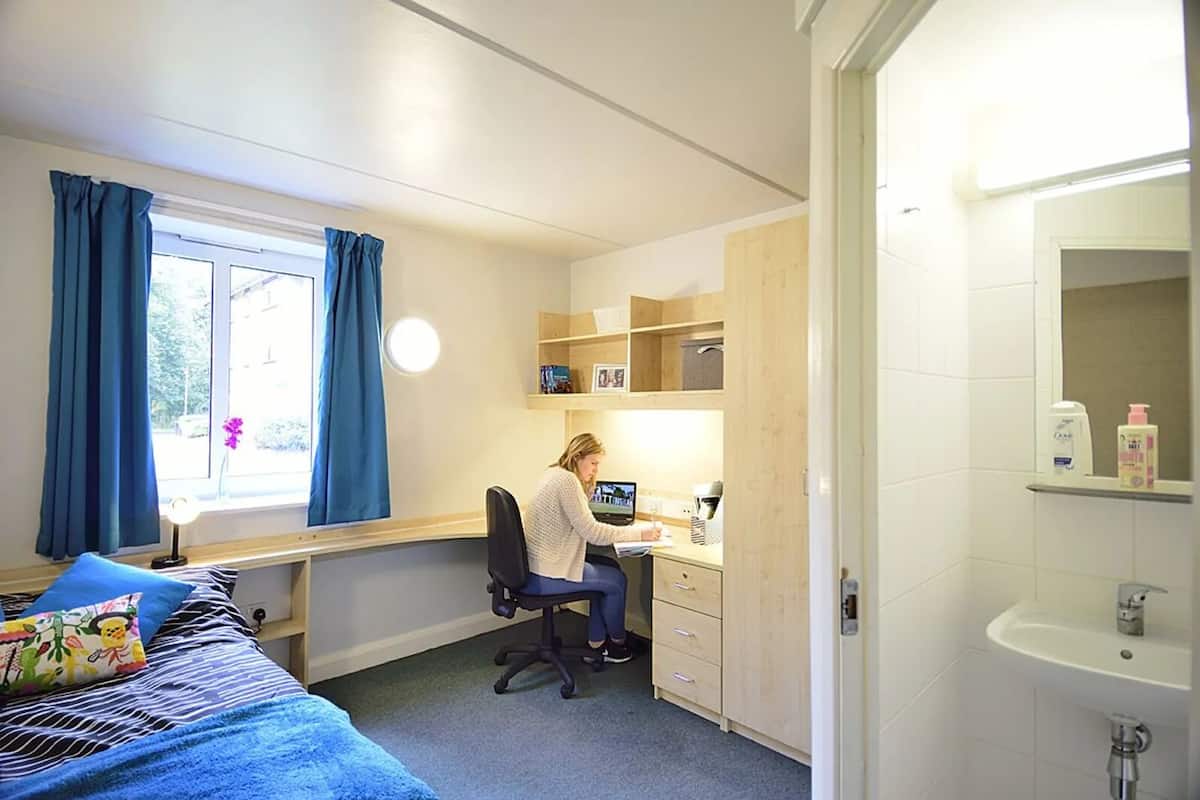 Un dormitorio con cama, escritorio, computadora y baño con lavamanos.