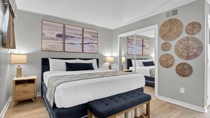 Un dormitorio moderno con una cama grande, mesitas de noche, un banco y cuadros en la pared.
