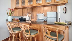 Una cocina con armarios de madera, una isla central con taburetes de bar, un refrigerador blanco y una cafetera.