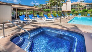 Una piscina con mosaicos azules, rodeada de sillas de descanso y palmeras.