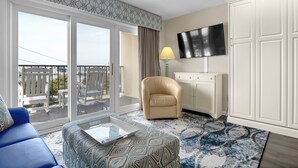 Moderni hotellihuone, jossa on parveke, sohva, tuoli, televisio ja työpöytä.