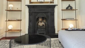 Un salón con chimenea, una mesa redonda negra y dos estanterías de madera con libros y adornos.