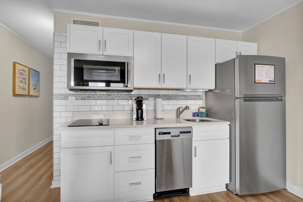 A compact kitchen with white cabinets, a stainless steel refrigerator, a built-in microwave, and a dishwasher. - Summer Sands- Who Let the Dogs In Room 305 (Wrightsville Beach)