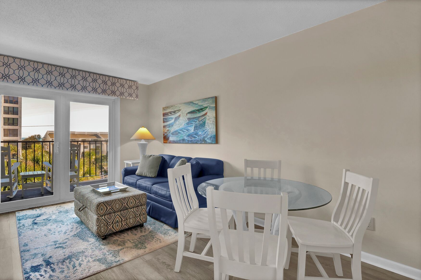 A modern living room with a blue sofa, white chairs, a glass table, and a painting on the wall.