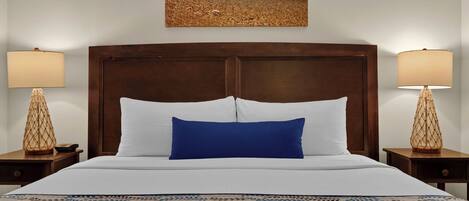 A hotel room with a large bed, two bedside lamps, a wooden headboard, and a beach-themed painting on the wall.