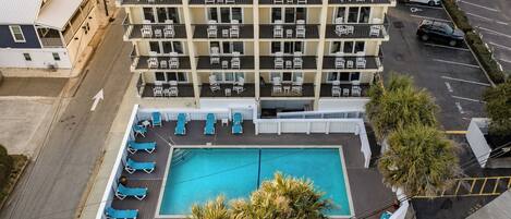 A multi-story hotel with a rooftop pool area, including lounge chairs and a swimming pool.